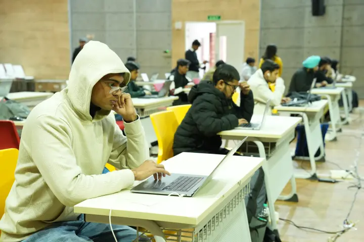 A player leaning in close to a laptop, a line of desks behind