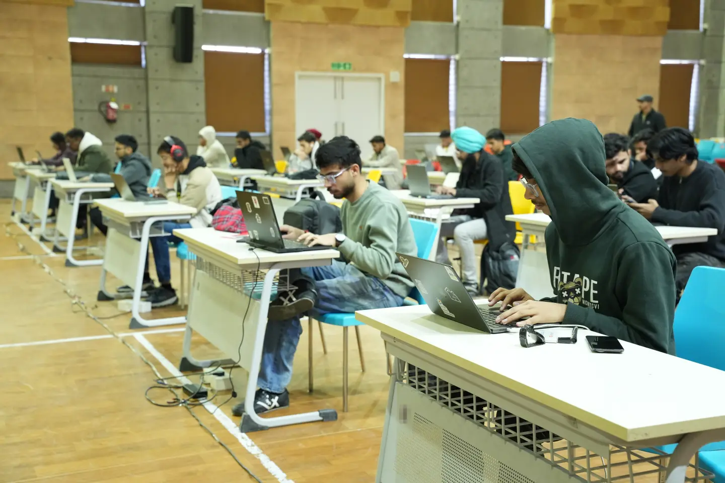 A long line of bench desks in a hall, around twenty-five people working at laptops