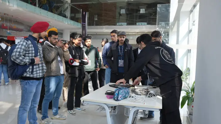 A ring of people standing round a table of small devices and cables