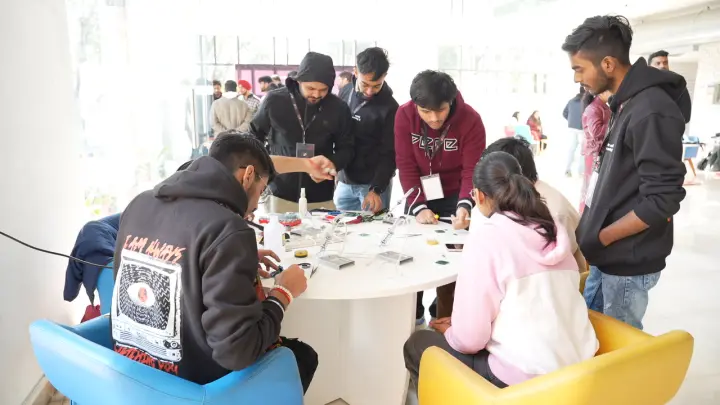 People crowded round a round table, leaning in over small boards and tools