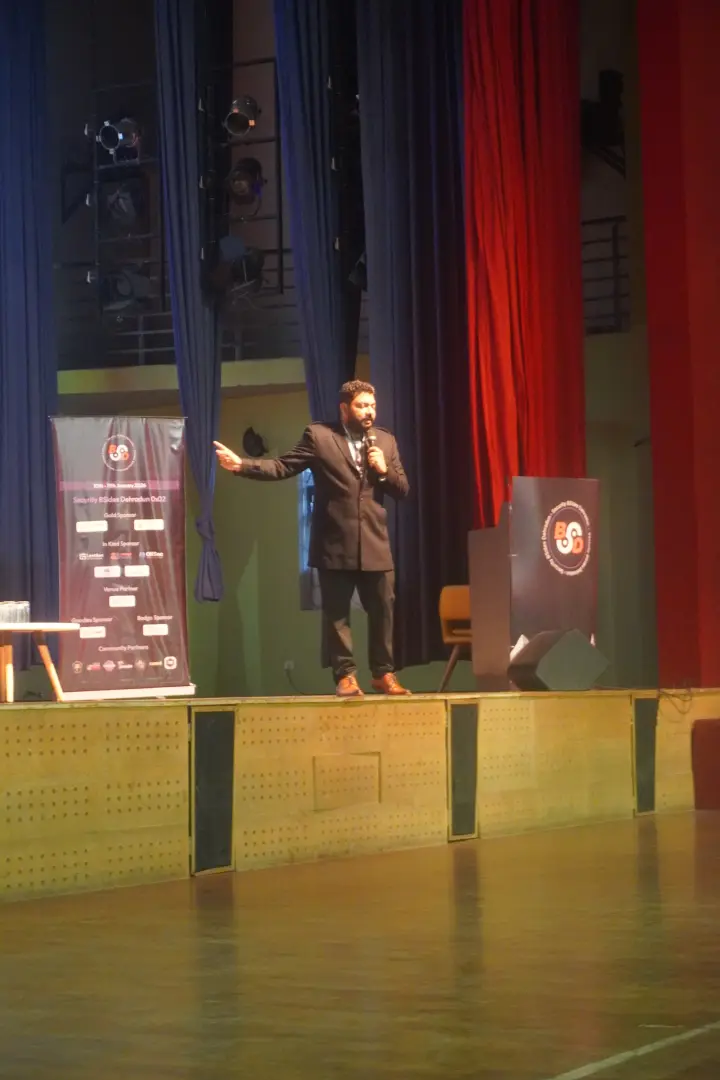 A speaker alone on a wide stage, microphone in one hand, arm open