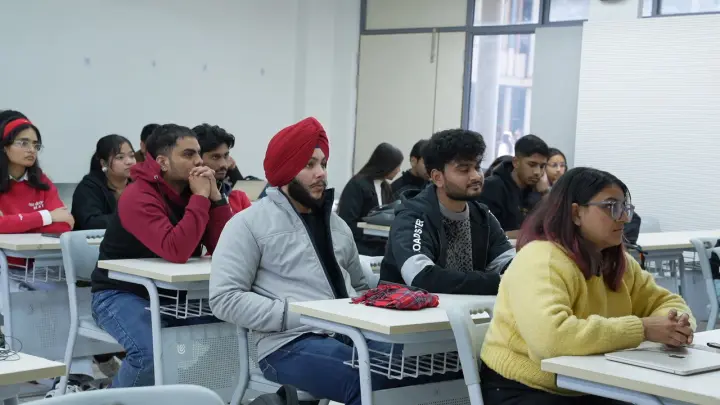 People at classroom desks, seen side on, following the session at the front